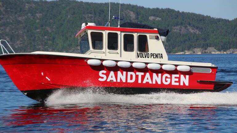 Rød servicebåt med Sandtangen-logo i fart på sjøen.